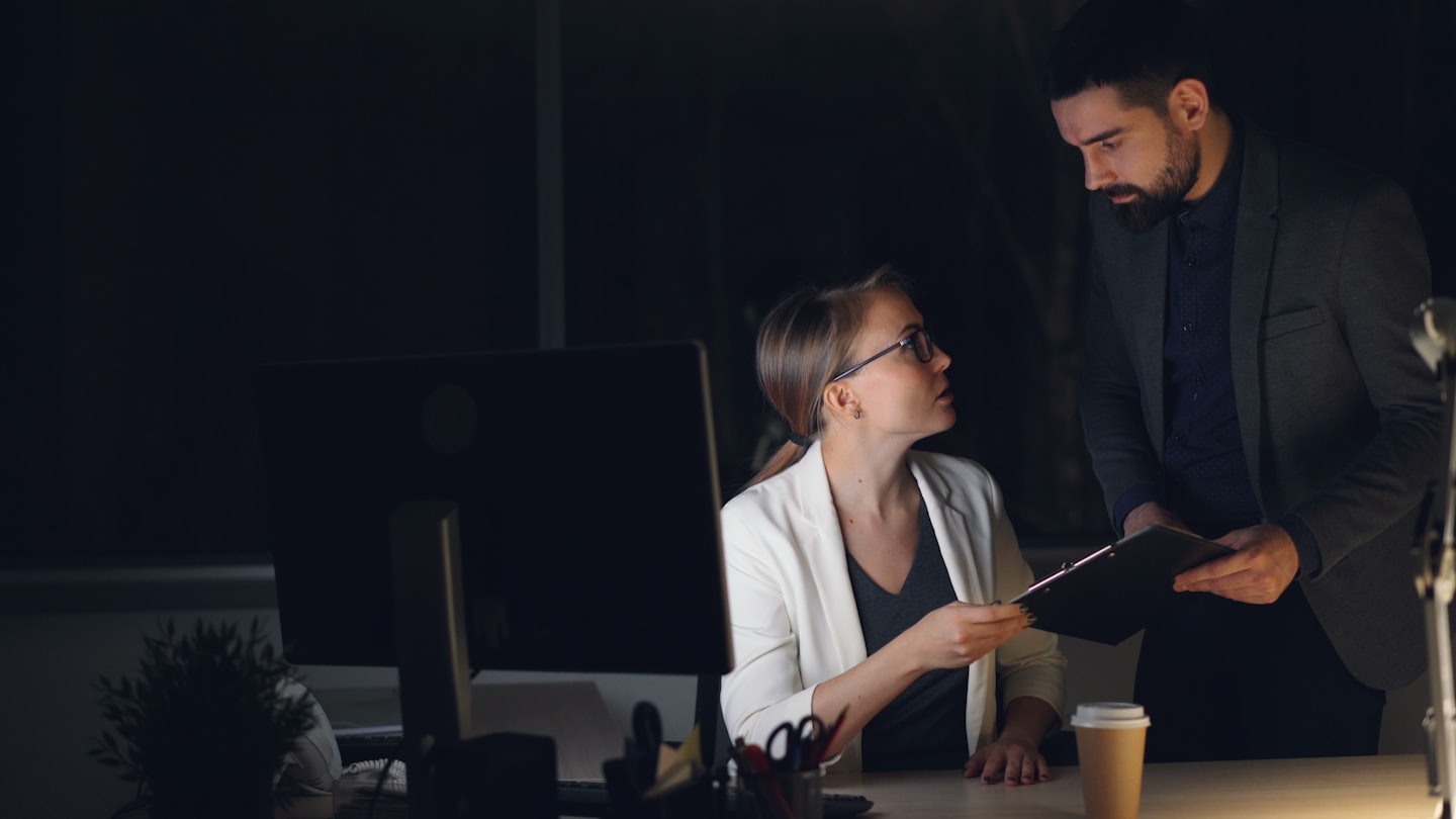 Business professionals discussing documents at a desk late at night.